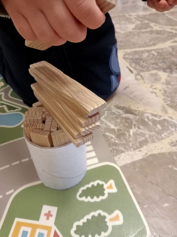 Le mani di un bambino che impilano legnetti sopra un tubo di cartone